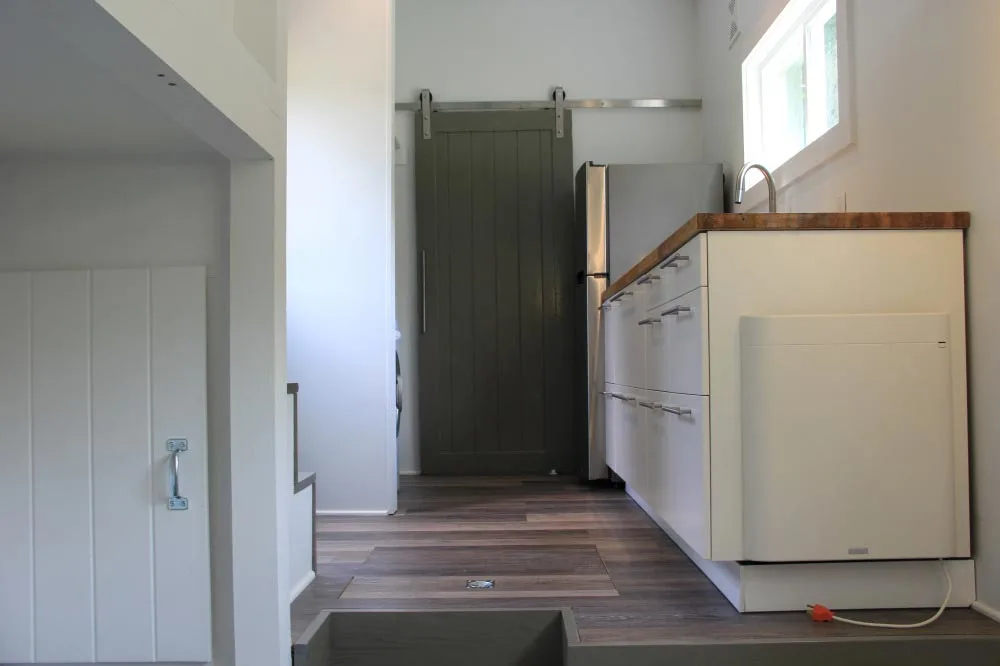 White kitchen cabinets and door to bathroom - Every Tiny Moment by Brevard Tiny House